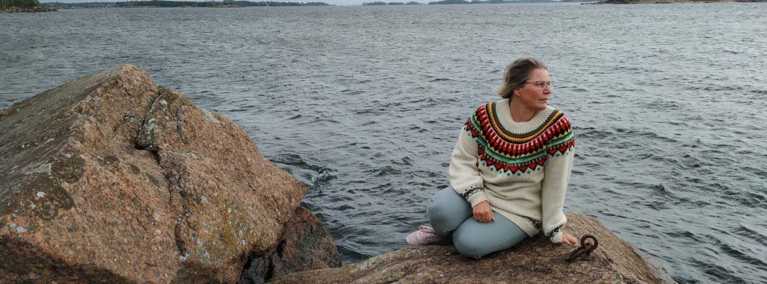 Wilhelmiina Kallio istuu kivellä veden äärellä
