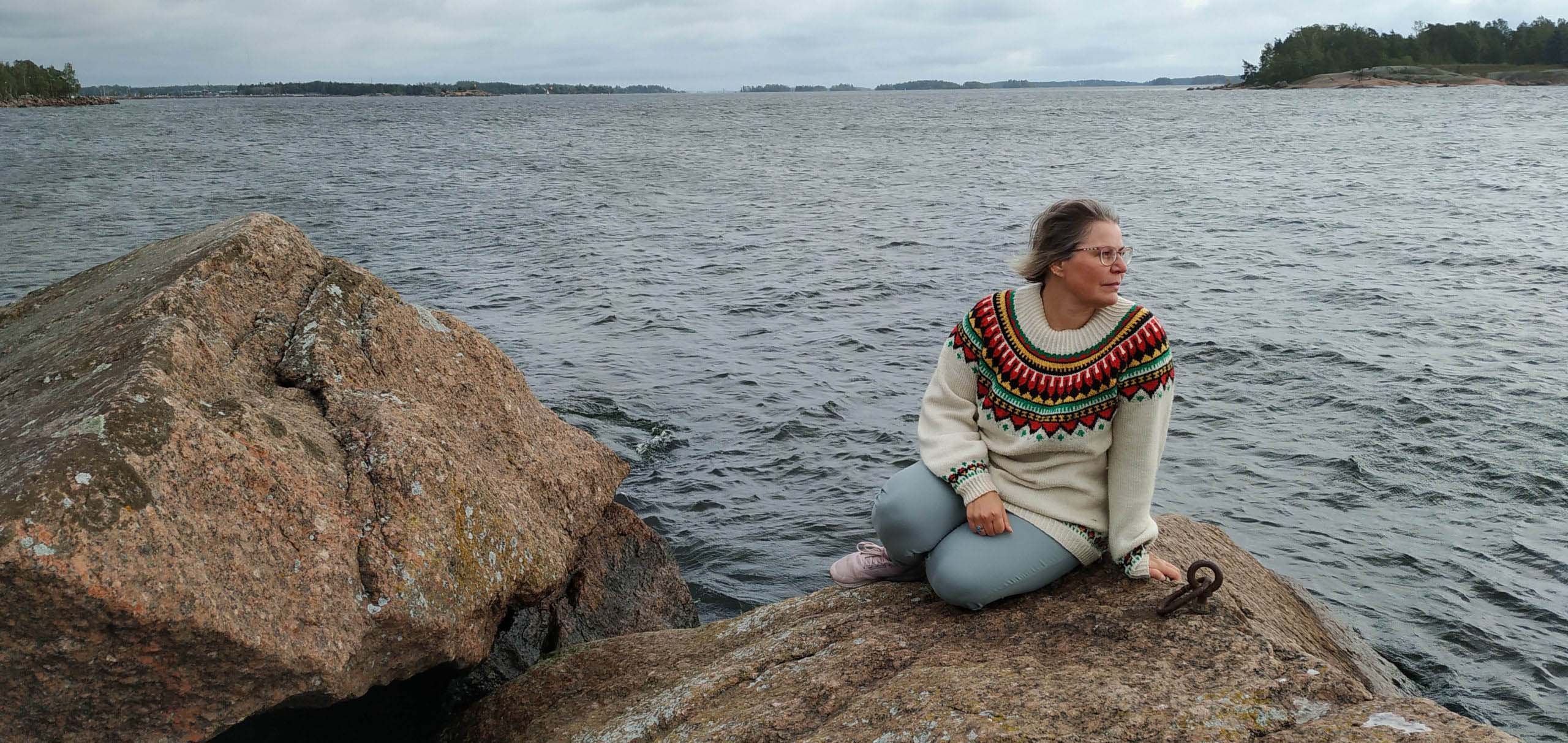 Wilhelmiina Kallio istuu kivellä veden äärellä