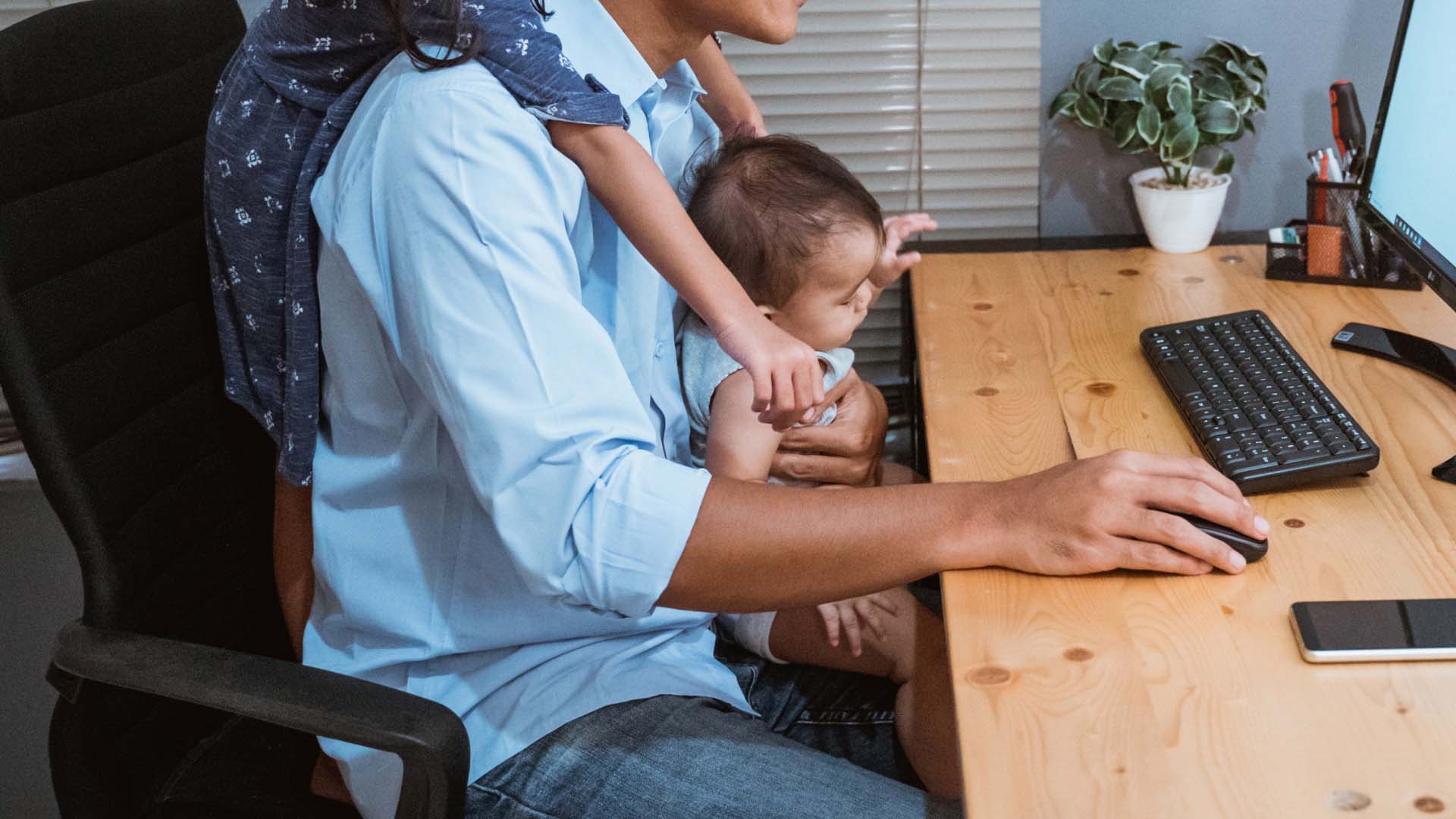Henkilö työskentelemässä tietokoneella ja lapsia hänen sylissään